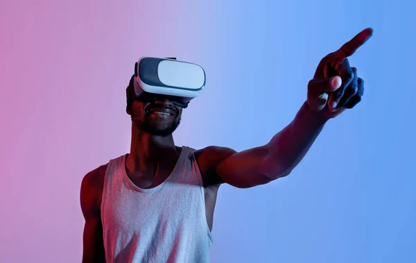 Oefenen met virtual reality. Jonge zwarte man in VR headset aanraken knop op denkbeeldig scherm in neon licht, mockup — Stockfoto