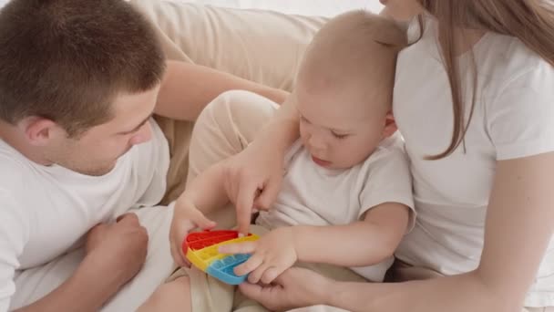 Adorable Infant Baby Playing With Pop It Toy While Relaxing With Parents — Stock Video