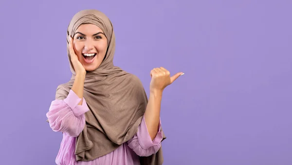Vaya, mira esto. Emocionada dama musulmana armenia en hijab apuntando al espacio libre sobre fondo púrpura, panorama — Foto de Stock