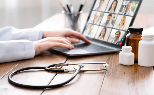 Жінка-лікар, використовуючи ноутбук, має відеочат з лікарями в приміщенні — стокове фото