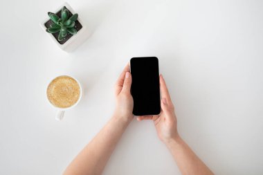 Beyaz ekranlı modern akıllı telefon kullanan ve elinde kahve fincanı olan bir kadın.