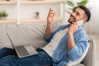 Bilgisayarda çalışan ve cep telefonuyla konuşan adam.