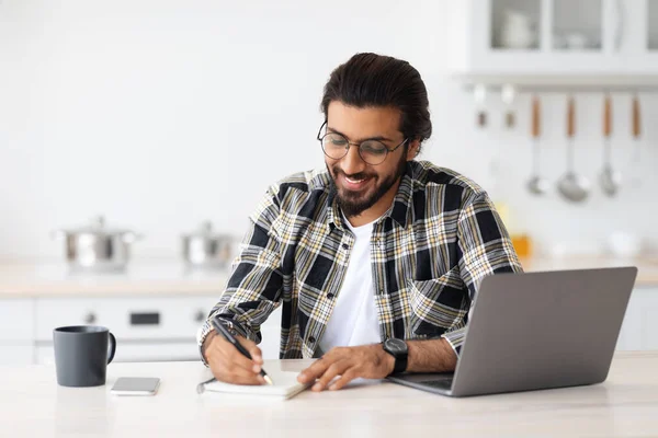 Positive arab guy looking for job online, kitchen interior