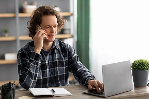 Vista lateral del tipo de negocios hablando por teléfono usando el ordenador portátil en interiores —  Fotos de Stock