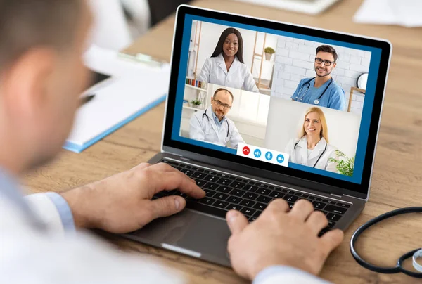 Senior Male Doctor Consulting Colleagues Via Video Call At Workplace — Stock Photo, Image