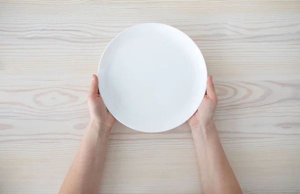 Mujer sosteniendo plato vacío esperando por la comida, sentado en la mesa de madera, vista superior, espacio para copiar —  Fotos de Stock