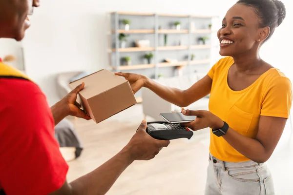 Afro-Amerikaanse klant vrouw betalende levering Guy met behulp van telefoon binnen — Stockfoto