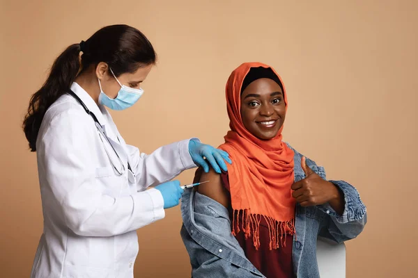 Mulher negra muçulmana no hijab sendo vacinada, mostrando o polegar para cima — Fotografia de Stock