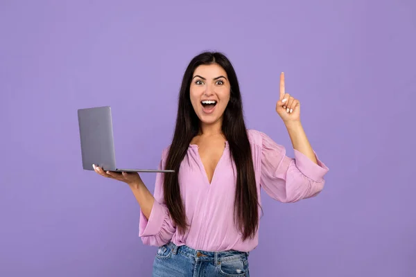 Femme arménienne excitée ayant idée créative, geste eureka avec ordinateur portable à la main, posant sur fond violet studio — Photo
