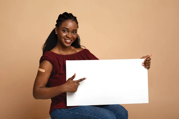 Вакцинация веселой африканской женщины, указывающей на чистый плакат, макет — стоковое фото