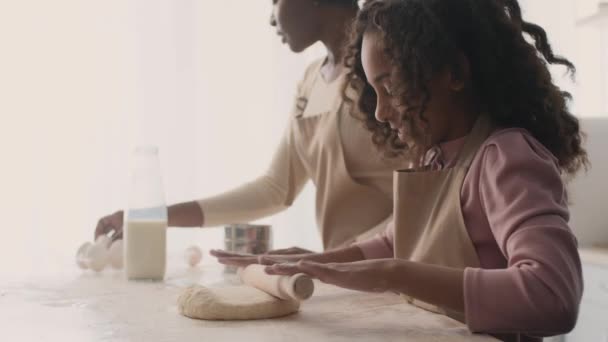 Carino poco afroamericano ragazza stendere pasta cruda con spillo di legno, preparare torta fatta in casa con la madre in cucina — Video Stock