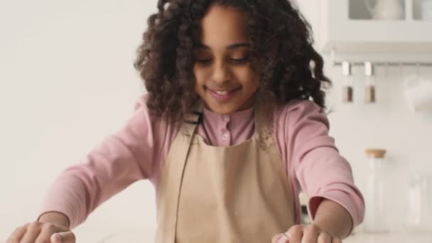 Közelkép portré a kis afro-amerikai lány roll out tészta a cookie-k, élvezi a főzési folyamat a konyhában — Stock videók