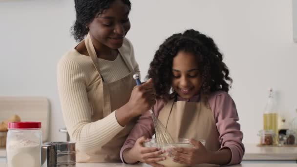 Afrikansk amerikansk mor och dotter kokar deg tillsammans i köket, kvinna tar smörja och knullar tjejer näsa — Stockvideo