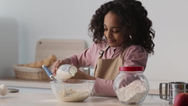 Ragazza afroamericana riccia che aggiunge latte ad altri ingredienti, preparando la pasta per la torta dolce in cucina — Video Stock