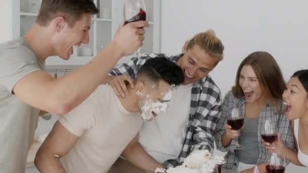 Cheerful multiethnic friends smashing birthday cake at mans face at home party — Stock Video