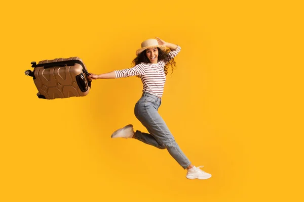 Vakantie tijd. Jonge opgewonden Arabische vrouw in rieten hoed springen met koffer — Stockfoto