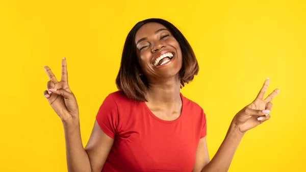 Glückliche schwarze Dame gestikuliert Sieg mit beiden Händen, gelber Hintergrund — Stockfoto