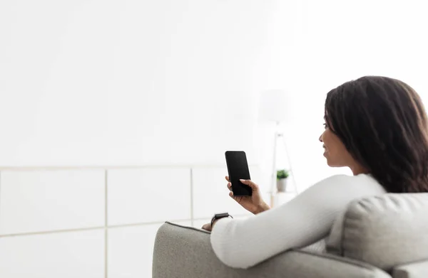 Temperatura del hogar, seguridad y control en la aplicación móvil. Mujer afroamericana usando teléfono inteligente, sentado en el sofá, espacio para copiar — Foto de Stock