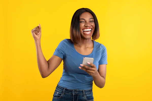 Feliz preto senhora segurando telefone Gesturing sim sobre fundo amarelo — Fotografia de Stock