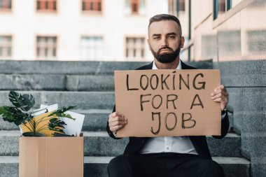 Bir iş arıyorum. Elinde kişisel eşyalar ve posterlerle merdivenlerde oturan olgun bir adam kriz yüzünden kovuldu.