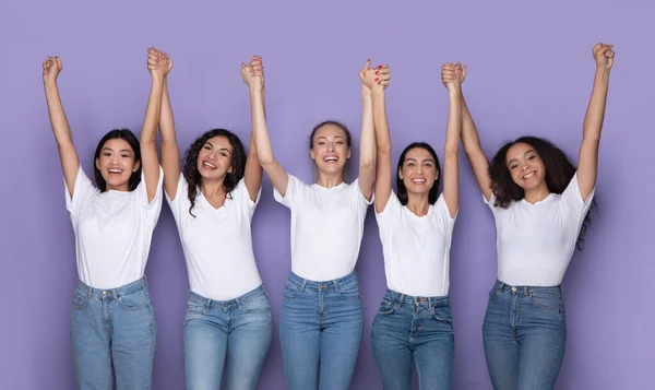 Alegre multiétnico senhoras segurando mãos posando juntos sobre roxo fundo — Fotografia de Stock