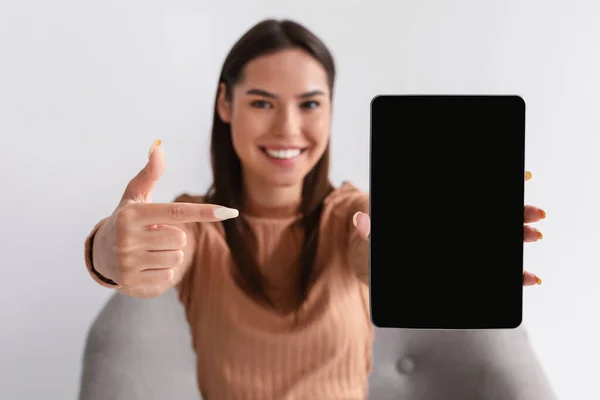 Mulher feliz apontando para tablet com tela em branco para mockup, apresentando novo aplicativo, oferecendo espaço para site ou anúncio — Fotografia de Stock