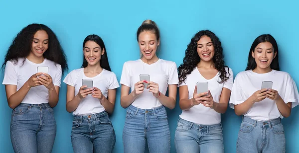 Cinco mulheres multirraciais felizes usando telefones em pé no fundo azul — Fotografia de Stock