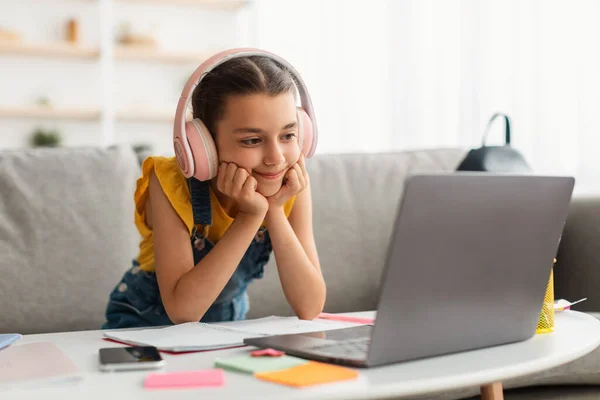 Chica sentada en el escritorio, usando portátil, con auriculares inalámbricos — Foto de Stock