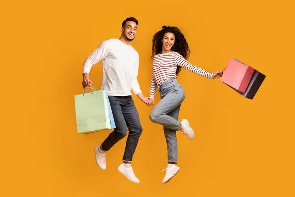 Conceito de vendas sazonais. Jovem e alegre casal árabe pulando com sacos de compras coloridos — Fotografia de Stock