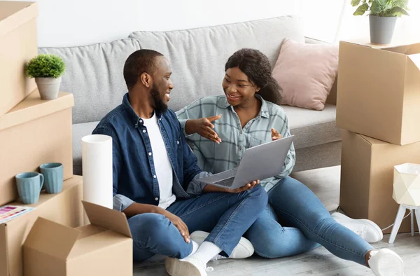 Cheerful Black Married Couple Sitting With Laptop Among Unpacked Cardboard Boxes — Stock Photo, Image
