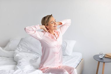Huzurlu bir kadın kollarını açıp yatağa oturuyor.