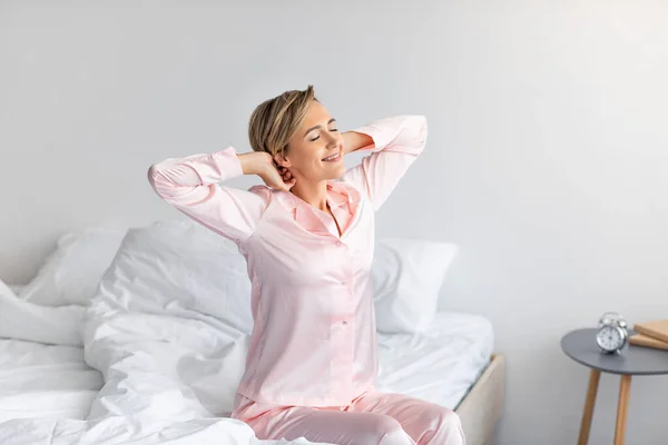 Mujer pacífica estirando los brazos y la espalda sentada en la cama —  Fotos de Stock