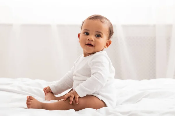 Afro-americano bebê infantil sentado na cama sorrindo em casa — Fotografia de Stock