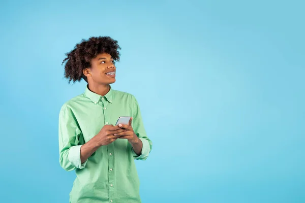 Oferta móvel. Feliz Africano americano adolescente cara segurando smartphone e olhando para o espaço livre no fundo azul — Fotografia de Stock
