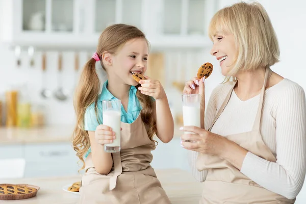 Süß klein mädchen und sie großmutter essen cookies trinken milch — Stockfoto