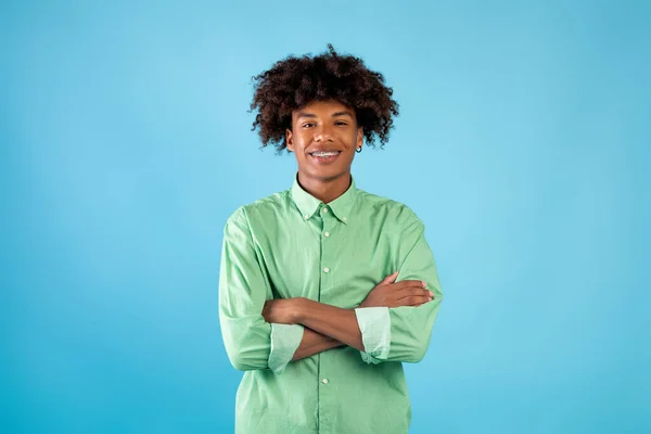 Portrait de jeune homme afro-américain avec les bras croisés regardant et souriant à la caméra, posant sur fond bleu — Photo