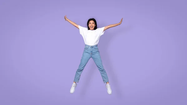 Carefree Aisan Young Lady Jumping Spreadeagle Over Purple Studio Background — Stock Photo, Image