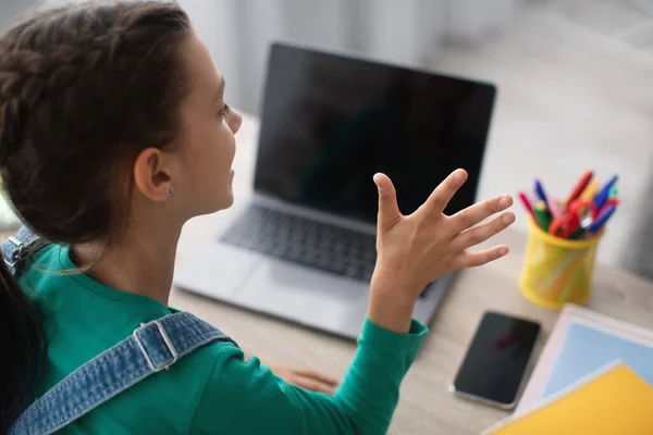 Menina sentada na mesa, usando laptop, acenando para webcam — Fotografia de Stock