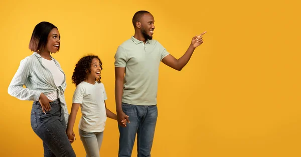 Positiva famiglia afro-americana di tre persone che guardano da parte, giovane che punta il dito contro lo spazio di copia su sfondo giallo — Foto Stock