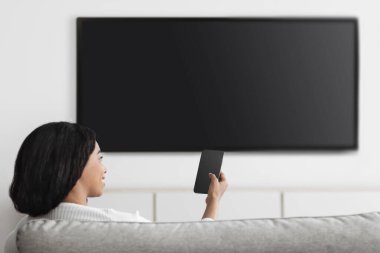 Akıllı telefon uygulaması tarafından kontrol edilen akıllı ev eğlencesi. Televizyona bağlı cep telefonu olan mutlu kadın, boş alan.