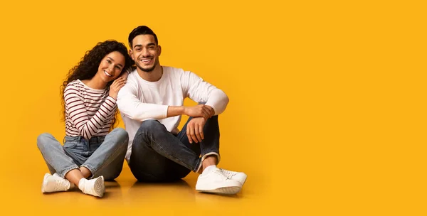 Щасливі Молоді Близькосхідні подружжя сидять на підлозі над жовтим тлом — стокове фото