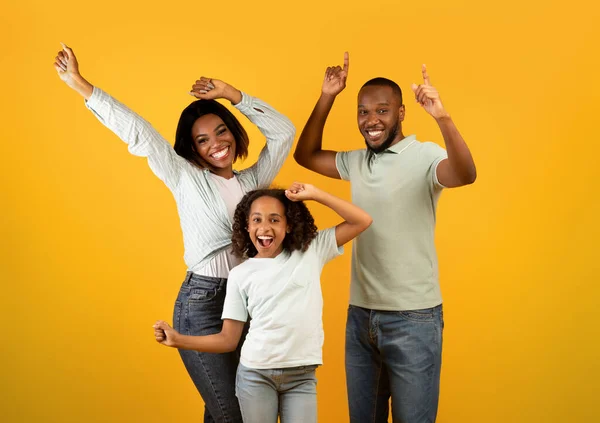 Alegre familia afroamericana de tres bailando y disfrutando de música favorita juntos en el fondo amarillo del estudio —  Fotos de Stock