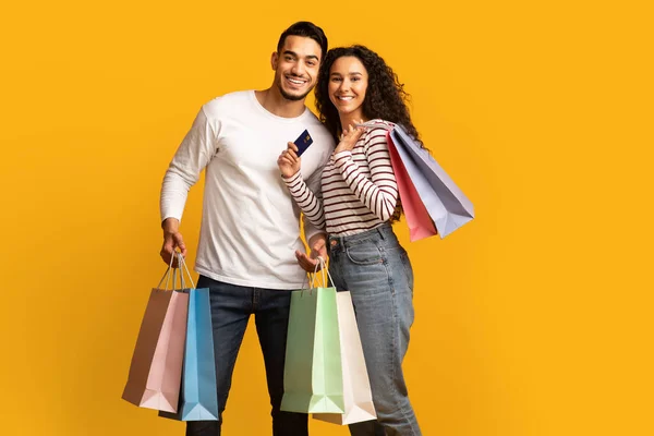 Jovem casal árabe alegre posando com cartão de crédito e sacos de compras brilhantes — Fotografia de Stock