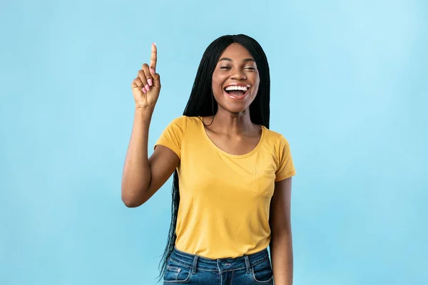Podekscytowana afrykańska kobieta wskazując palec w górę mając pomysł, niebieskie tło — Zdjęcie stockowe