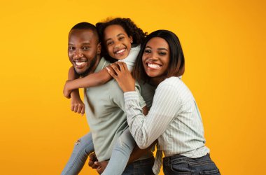 Aileyle zaman geçirmek. Aşırı neşeli Afro-Amerikan ailesi sarı stüdyo duvarında izole edilmiş kameralara gülüyor ve poz veriyor.