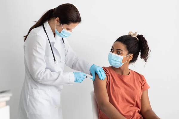 Enfermeira em roupa de trabalho branca fazendo vacinação para senhora negra — Fotografia de Stock