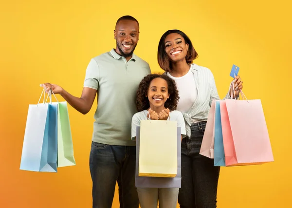 Familie winkelen. Opgewonden Afrikaanse Amerikaanse ouders en hun schattige dochter houden shopper tassen over gele achtergrond — Stockfoto