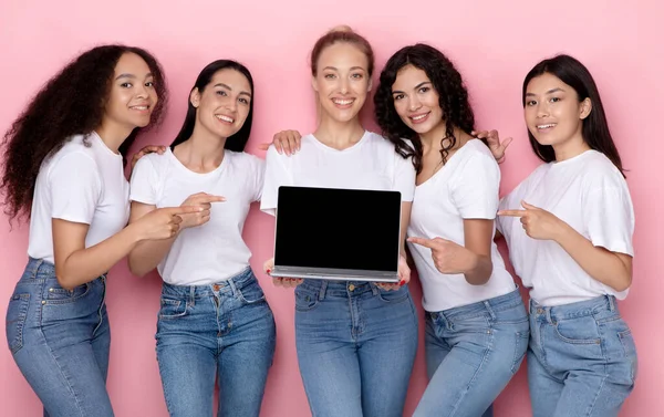 Diversas mujeres sosteniendo el ordenador portátil apuntando a la pantalla vacía, fondo rosa — Foto de Stock