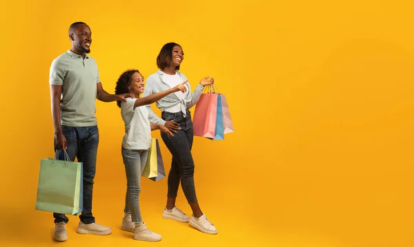 Familie winkelen. mooi meisje wijzend vinger naar vrije ruimte, tonen iets aan ouders, gele achtergrond, panorama — Stockfoto