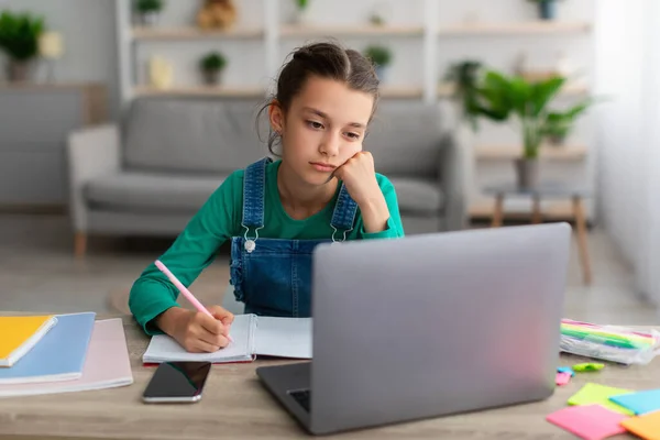 Chica de la escuela cansada escribiendo en el cuaderno haciendo la tarea — Foto de Stock